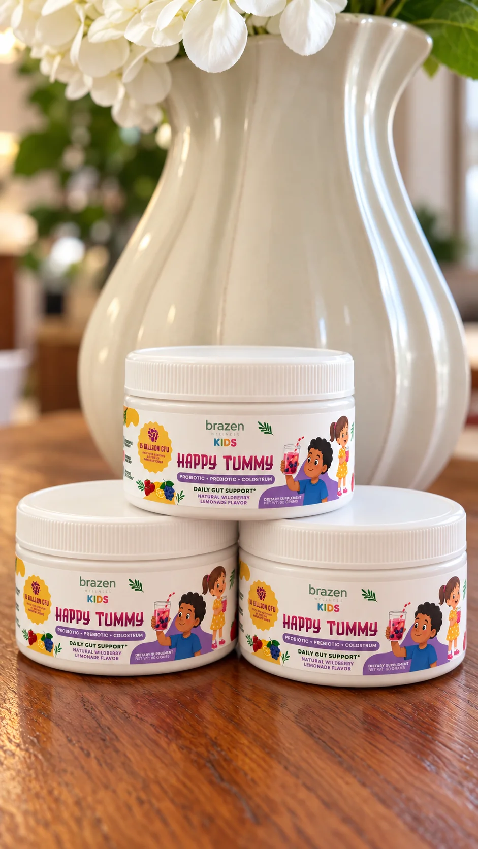 Three tubs of Brazen Kids Happy Tummy stacked on a wooden table in front of a white vase of flowers